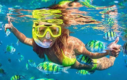 woman with a snorkel mask swimming next to bright yellow fish 